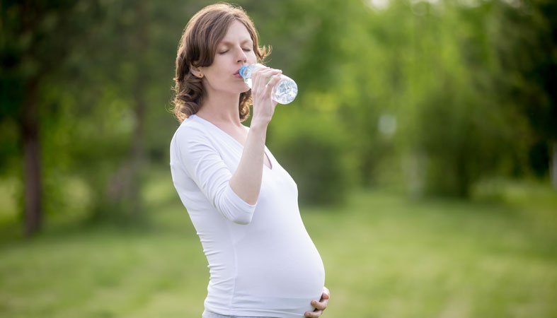 pregnant woman is drinking water in nature