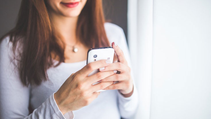A woman is holding her mobile phone with both hands