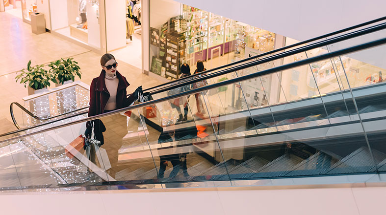 Lady with the glasses on her face is standing on the escalator in the shopping mall