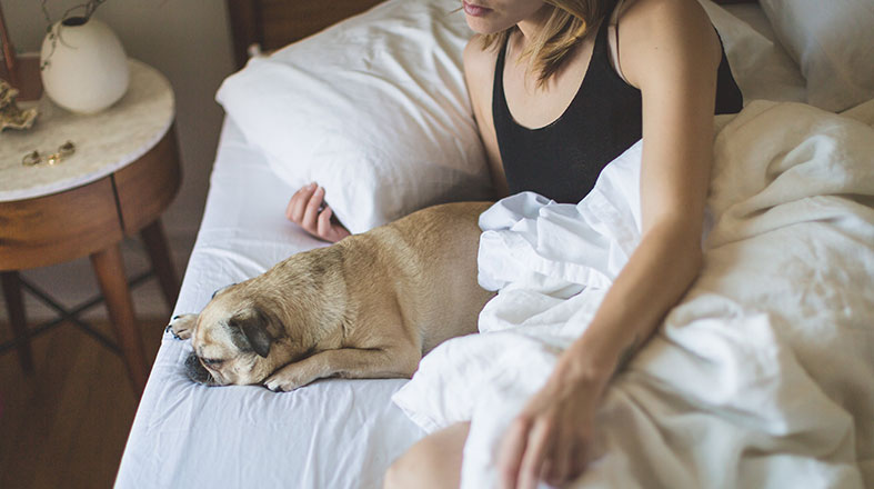 woman is laying on the bed with her little dog next the her