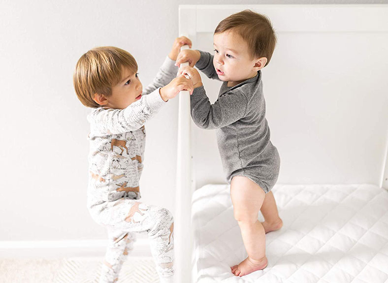two cute toddlers are playing in the crib