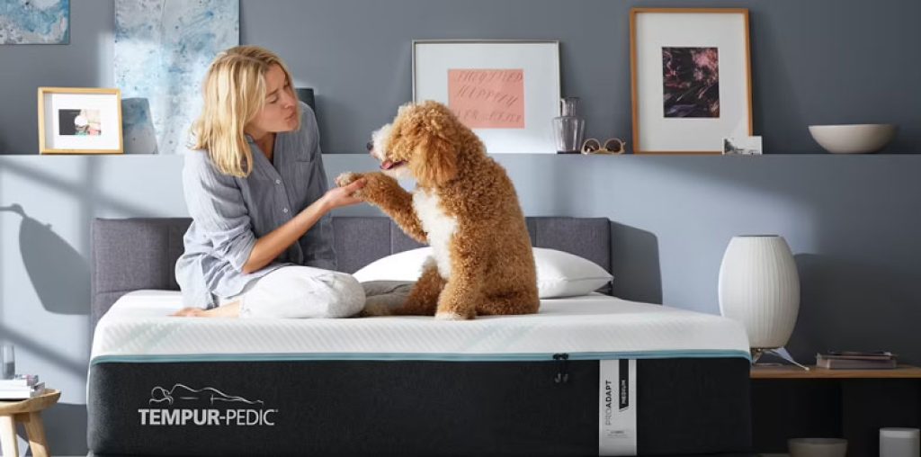 a lady and a dog are sitting on the tempur-adapt bed